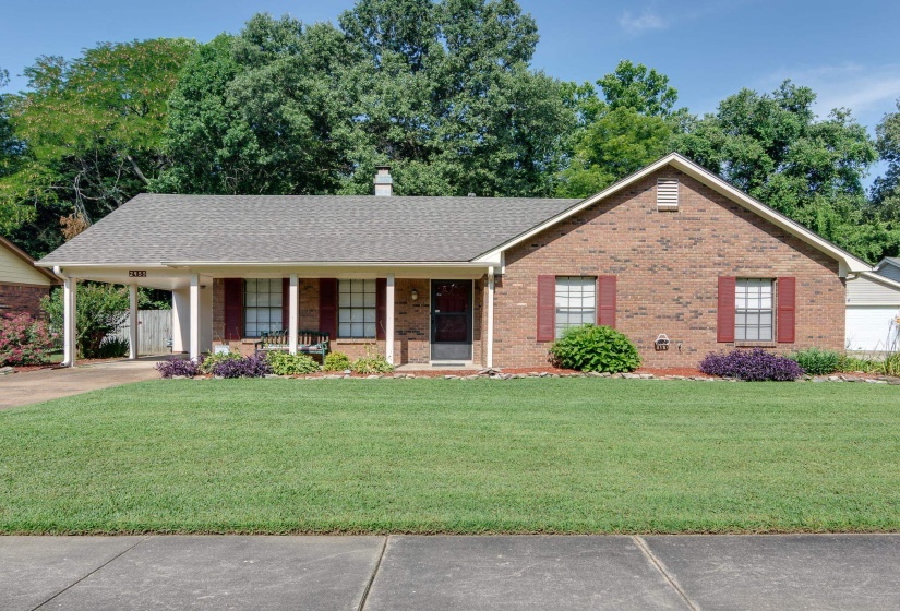 Brick facade home with a covered carport, mature landscaping, and red window shutters