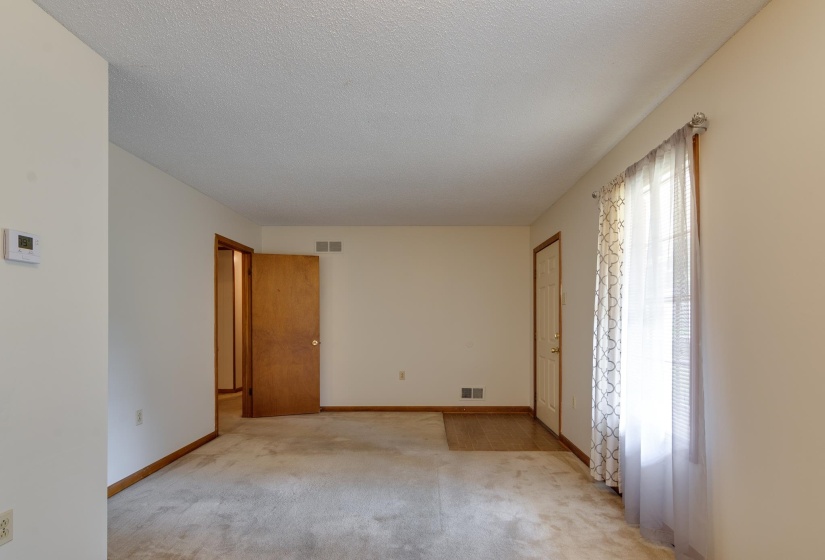 Carpeted room featuring a window with vertical blinds and sheer curtains, a solid wood door, and a thermostat