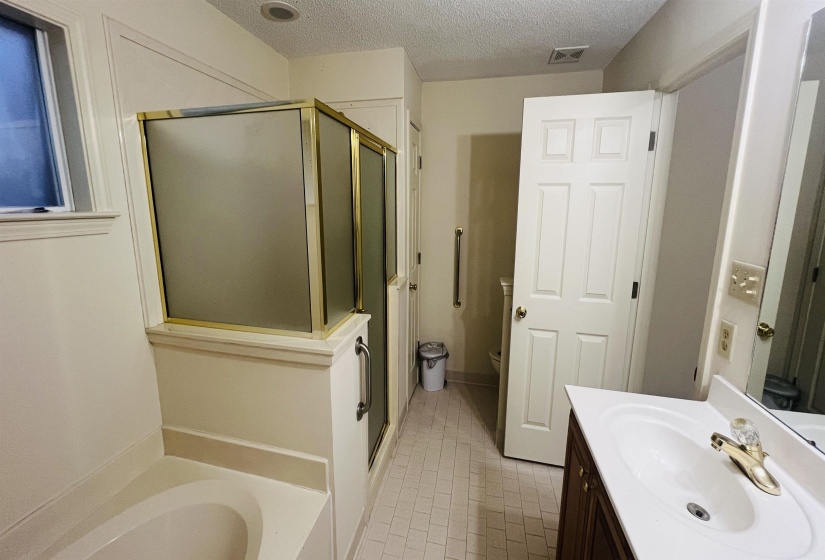 Bathroom featuring a built-in tub, a shower enclosure with a gold-toned frame, an integrated vanity with a single basin sink, and tile flooring