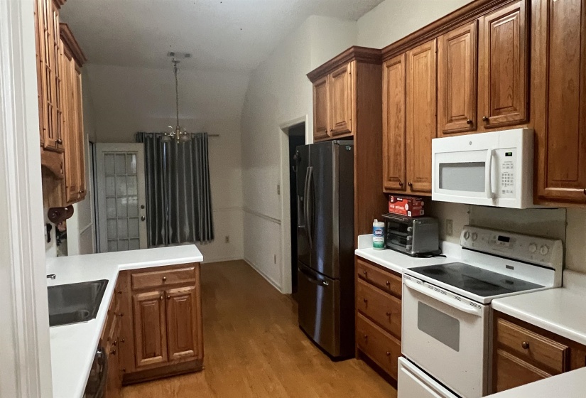 Kitchen featuring wood-finish cabinetry, white countertops, built-in stainless steel refrigerator, white range, and wood-finish flooring