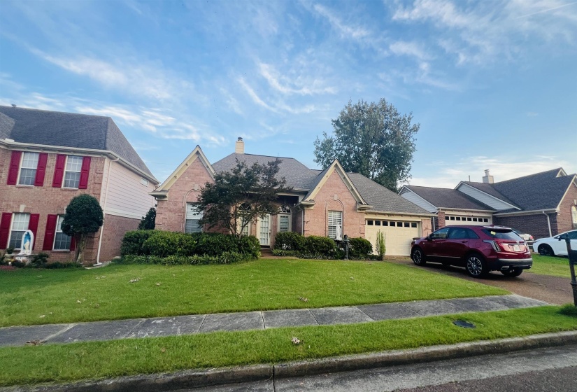 Brick facade single-story home with an attached multi-car garage, established front landscaping, a paved driveway, and a shingled roof