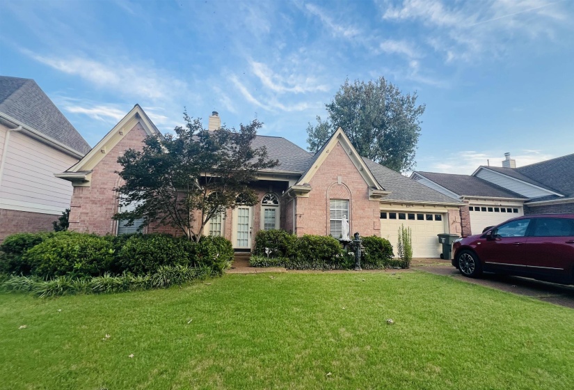 Brick exterior with a gabled roofline, mature front yard landscaping, and a multi-car garage with white doors