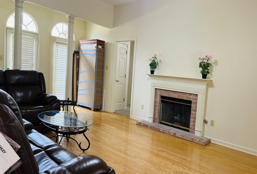 Living area featuring a brick fireplace with a white mantel, light wood-finish flooring, and arched windows with columns