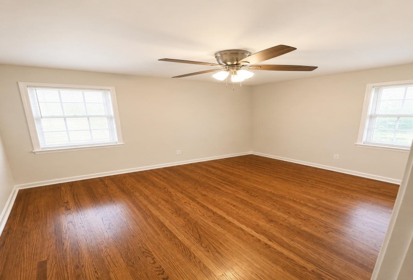Spacious room featuring a stone fireplace with hearth, integrated built-in shelving, triple windows, and a ceiling fan