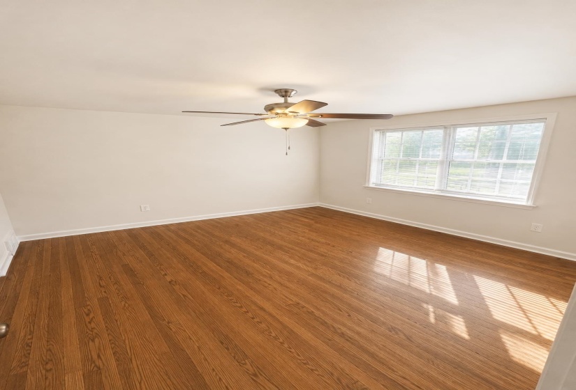 Spacious room with wood-finish flooring, a ceiling fan with integrated lighting, and white walls