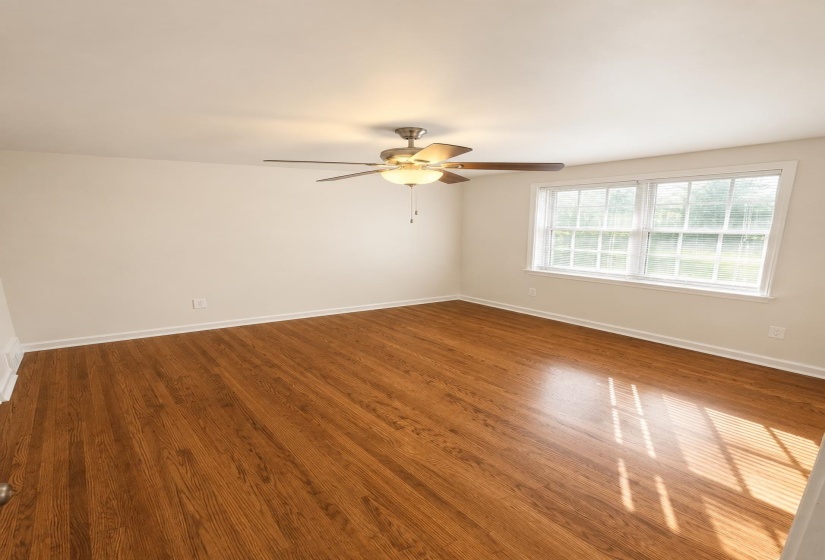 Bright interior room featuring wood-finish flooring, a ceiling fan with light fixture, and a large window with white blinds