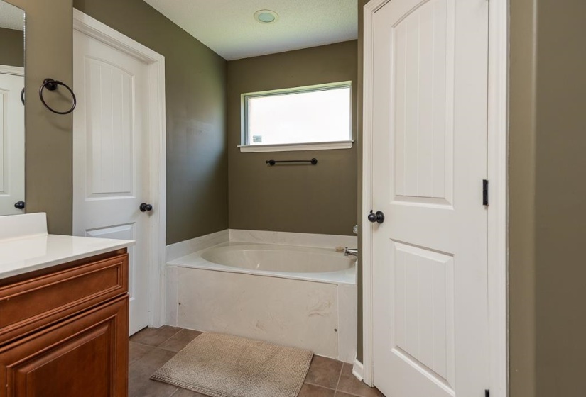 Bathroom featuring a built-in soaking tub beneath a window, updated wood-finish vanity with a light-colored countertop, and recessed lighting. To right of picture is door to the private toilet closet.