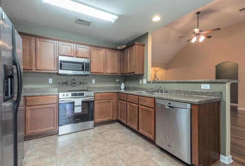 Kitchen featuring wood-finish cabinetry, stainless steel appliances, Formica Laminate countertops, and tile flooring. Lots of Drawer and Cabinet Space, Opens to Great Room and Eat-In Kitchen Area.