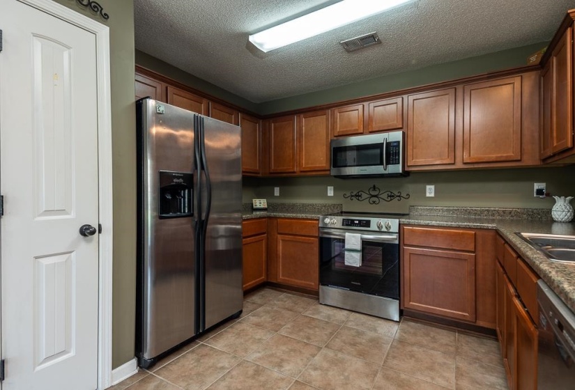 Kitchen featuring wood cabinetry, stainless steel appliances, tiled flooring, and Formica Laminate countertops.