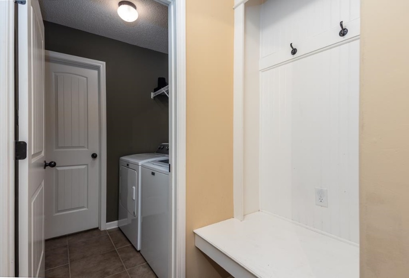 Laundry area with ceramic tile flooring, built-in shelving, and a nearby mini-mudroom bench with wainscoting and coat hooks.