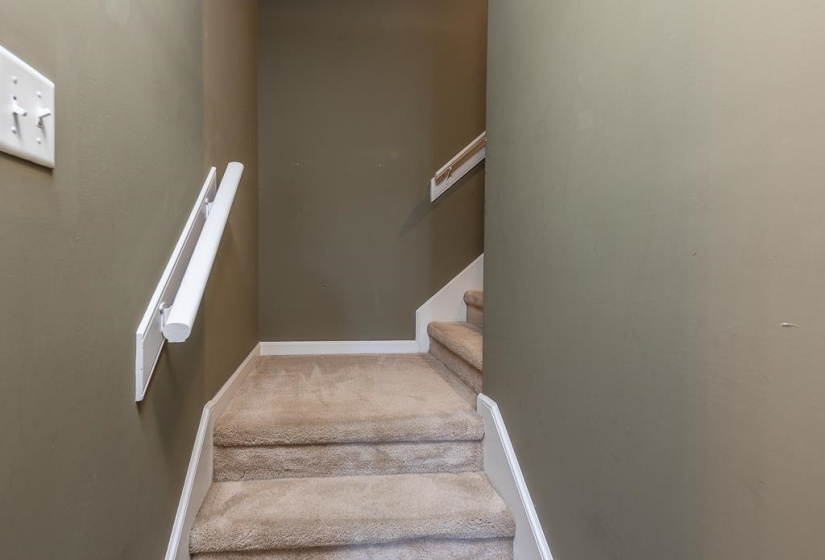 Carpeted staircase featuring painted walls, white baseboards, and wall-mounted handrails