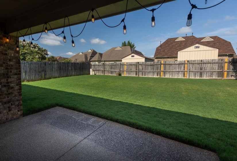 Covered patio with string lighting, exposed aggregate concrete flooring, brick column, and a fully fenced backyard with a manicured lawn!