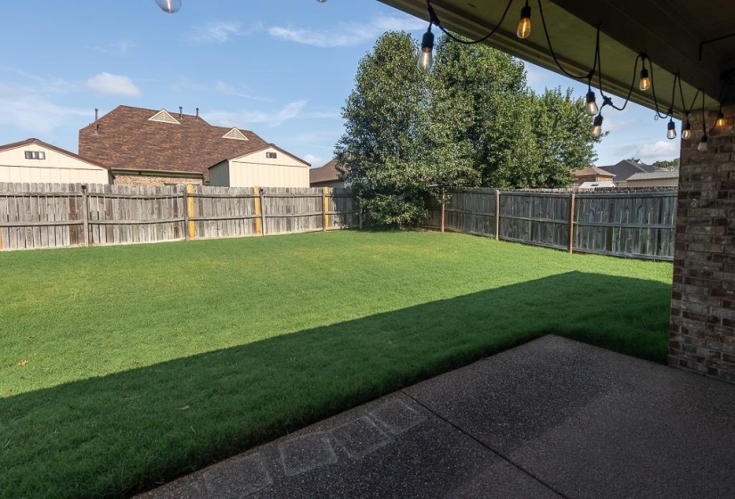 Expansive backyard featuring a lush lawn, privacy fencing, and a concrete patio