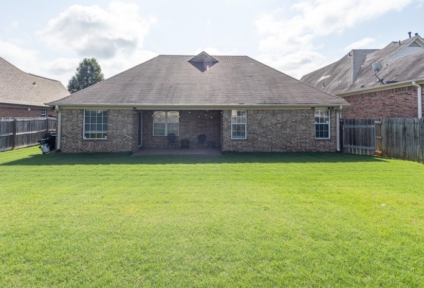 Spacious backyard featuring a large green lawn, a covered patio, and a privacy fence