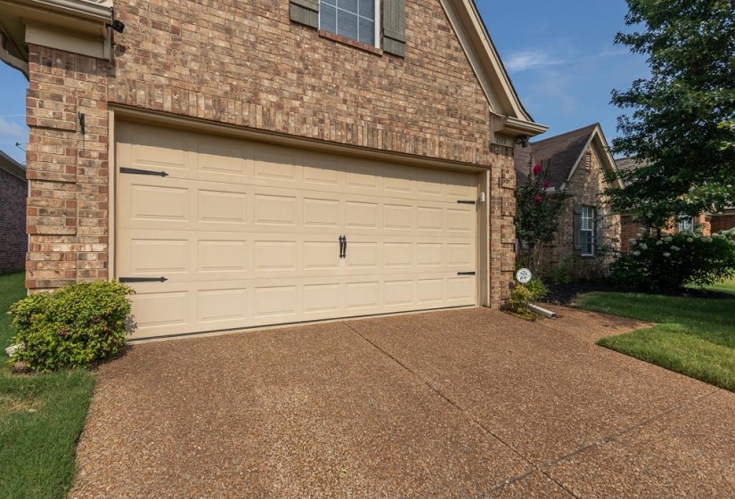 Two-car garage with a panel-style door and decorative hardware, complemented by a textured aggregate driveway
