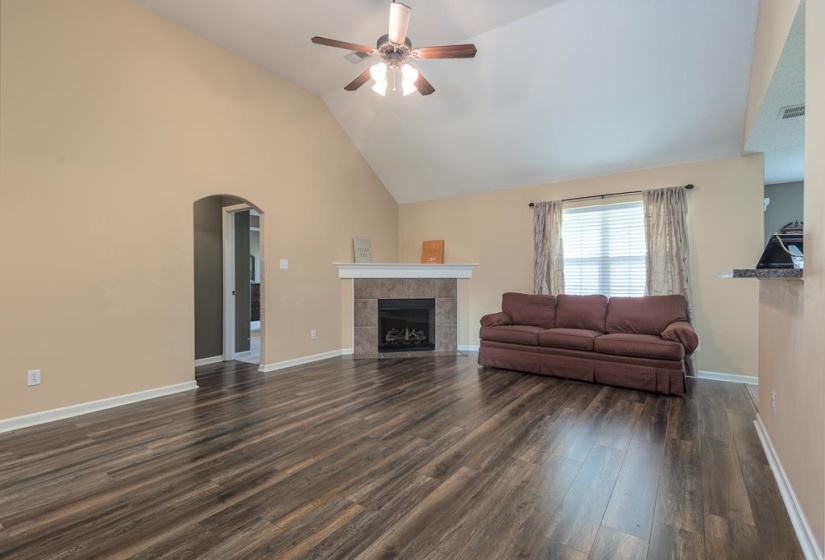 Vaulted ceiling living area featuring LVP Flooring, a tiled fireplace with a mantel, and an arched doorway to Primary Suite and Stairway to Bonus Room.