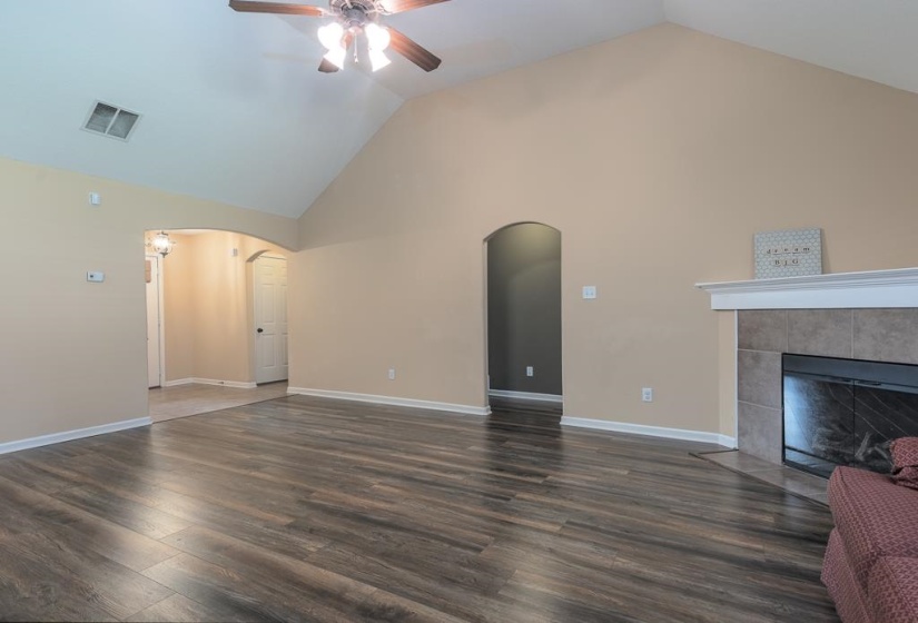 Spacious living area featuring wood-finish flooring, a vaulted ceiling, and an arched entryway