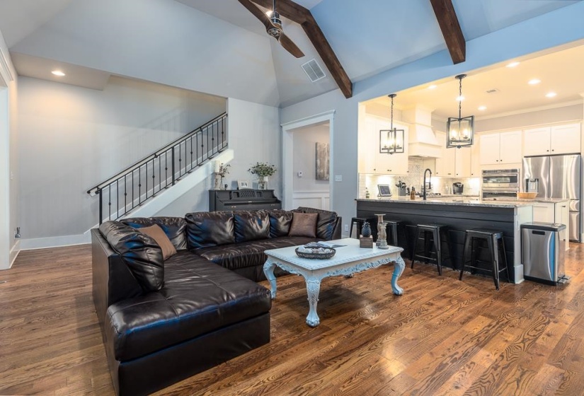Open-concept living space featuring wood-finish flooring, vaulted ceilings with exposed beams, and recessed lighting