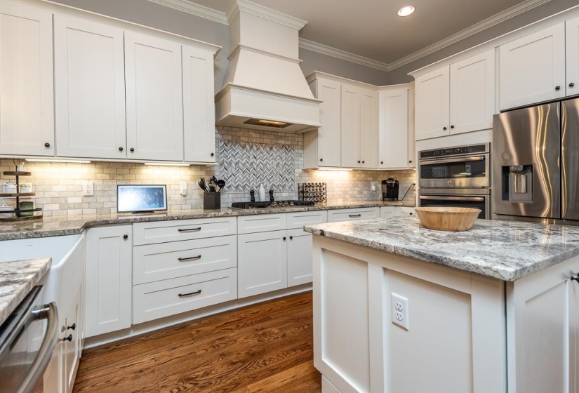 Kitchen featuring white shaker cabinetry, an island with a stone countertop, a tile backsplash, wood-finish flooring, and stainless steel appliances