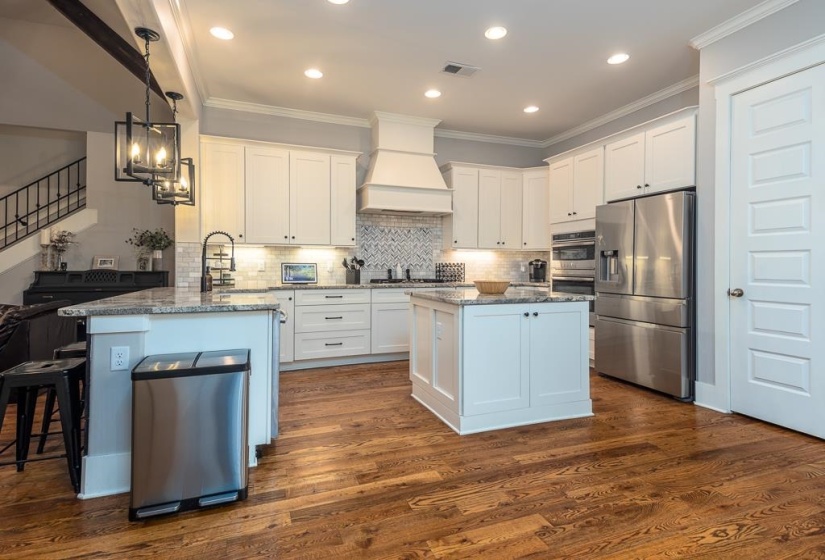 Contemporary kitchen featuring white cabinetry, a center island, stainless steel appliances, granite countertops, and wood-finish flooring