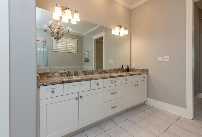 Double vanity with white shaker cabinetry, stone countertop, dual sinks, and two wall-mounted light fixtures