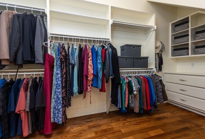 Custom closet system featuring wood-finish flooring, multiple hanging rods, open shelving, and built-in drawers