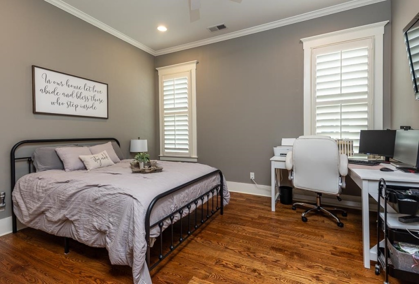 Interior room featuring wood-finish flooring, crown molding, and two windows with white plantation shutters