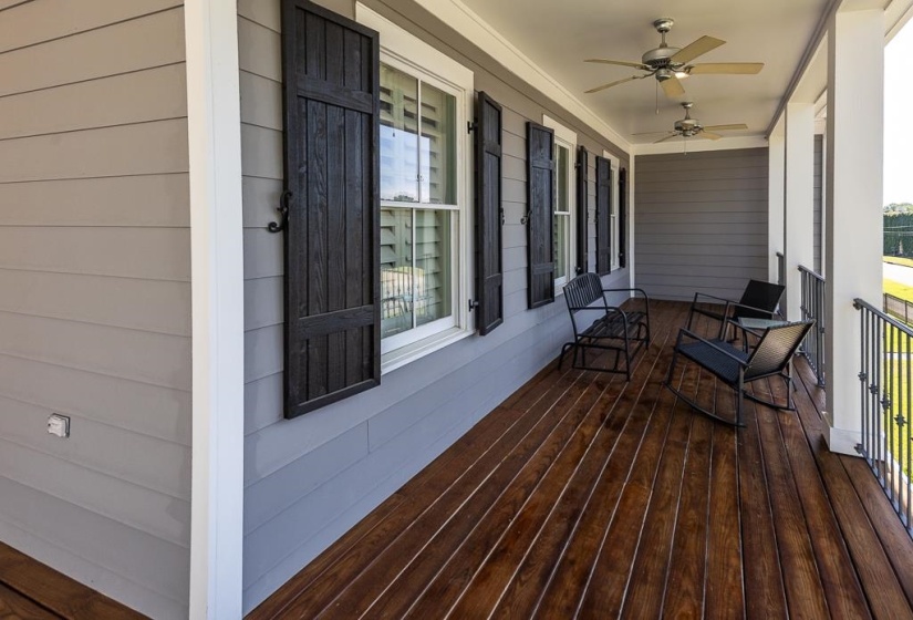 Expansive covered porch featuring rich wood-finish flooring, multiple ceiling fans, gray horizontal siding, and decorative black window shutters