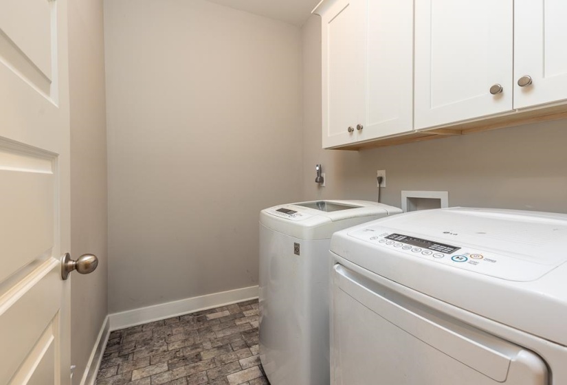 Laundry area featuring white cabinetry with brushed nickel hardware, light neutral wall paint, and stone-look tile flooring