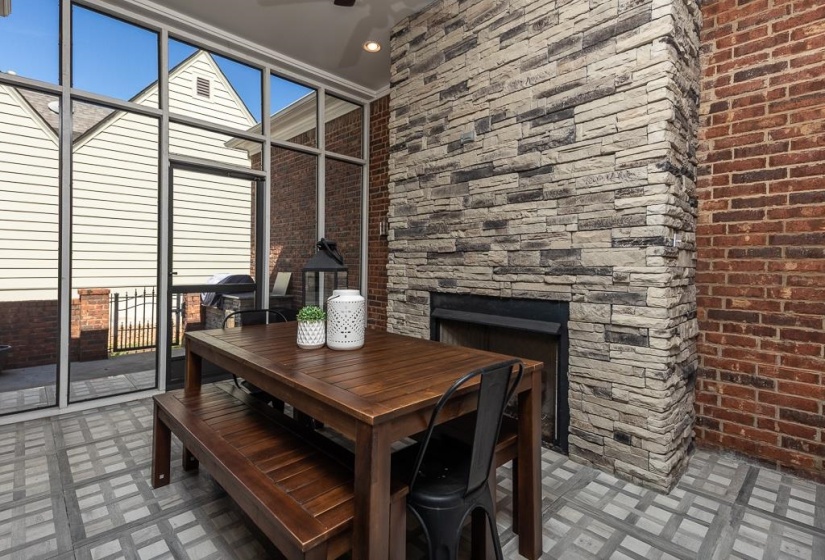 Screened outdoor living space featuring a stone gas fireplace, brick accent wall, and tiled flooring