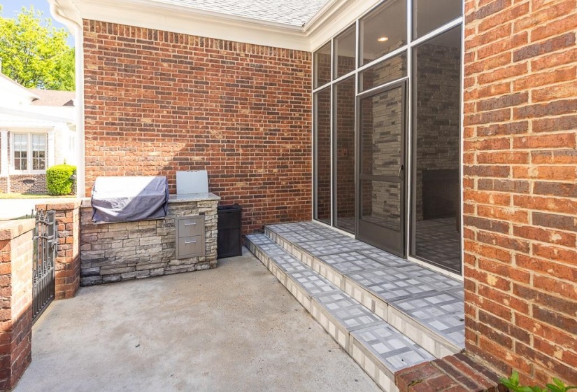 Expansive concrete patio with a built-in outdoor kitchen featuring stone veneer, a light-toned countertop, and stainless steel drawers