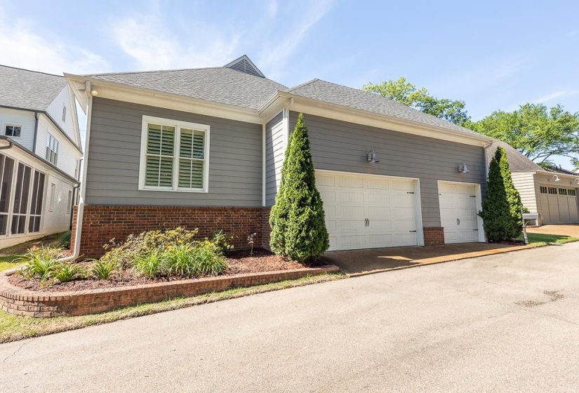 Three-car garage with white paneled doors, gray siding, and brick foundation