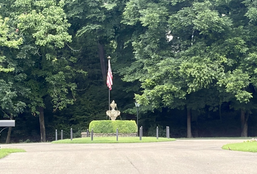 Circular drive featuring a central fountain, manicured hedges, and mature trees