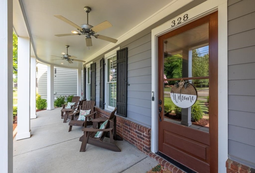 Inviting covered front porch with multiple ceiling fans, gray siding, brick foundation, and dark wood shutters