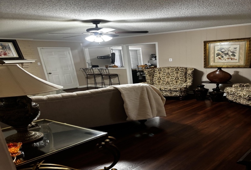 Living area featuring wood-finish flooring, a ceiling fan with integrated lighting, and crown molding