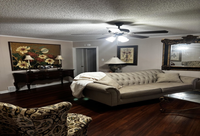 Living space featuring rich wood-finish flooring, crown molding, and a ceiling fan with integrated lighting