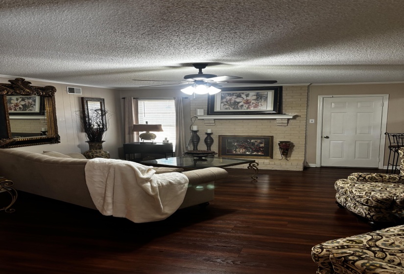 Living area featuring dark wood-finish flooring, a ceiling fan with integrated lighting, a brick fireplace, a built-in mantel, and light-colored wall paint