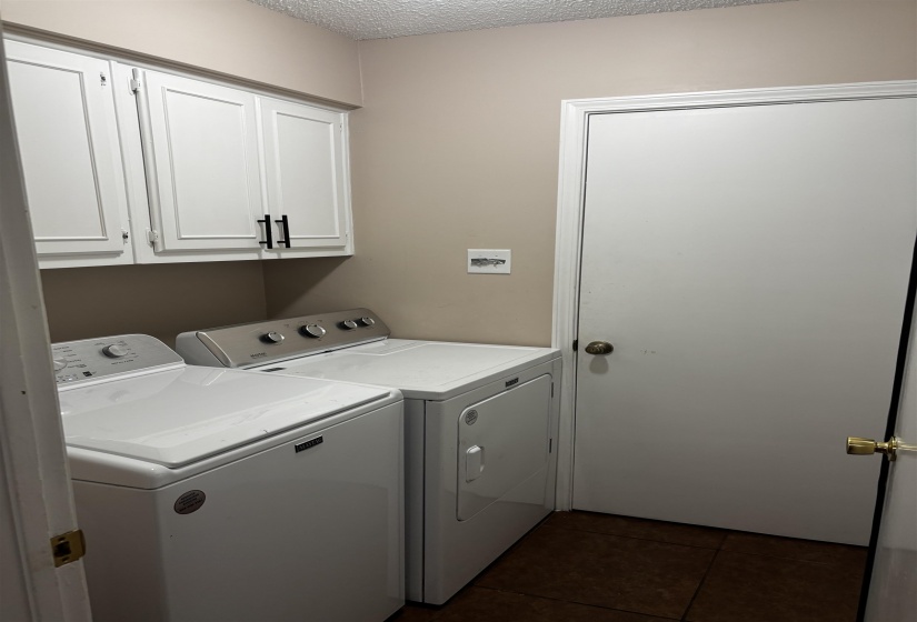 Laundry area featuring white shaker-style cabinetry with matte black pulls, beige wall paint, and dark tile flooring