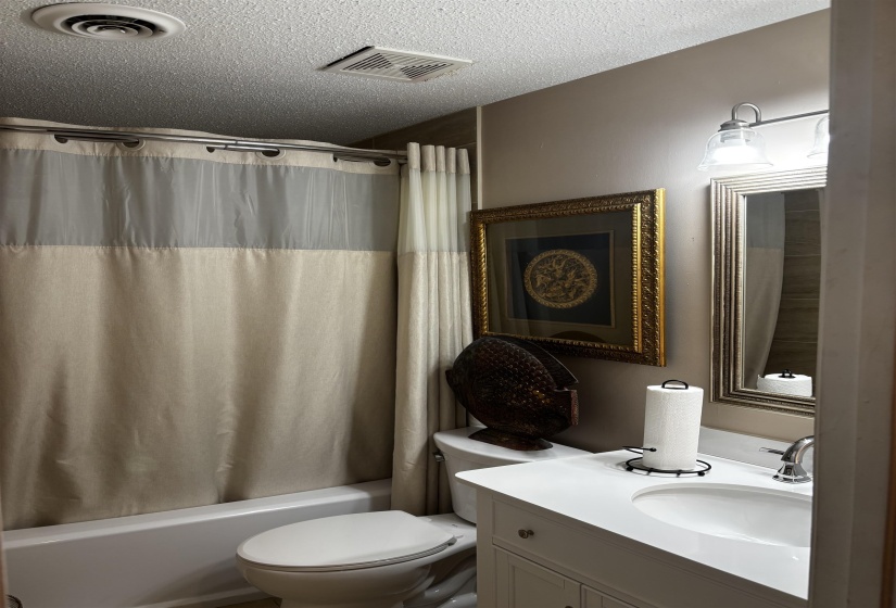 Bathroom featuring a white bathtub with a shower, a toilet, a vanity with a white countertop and integrated sink, a chrome faucet, and a wall-mounted mirror
