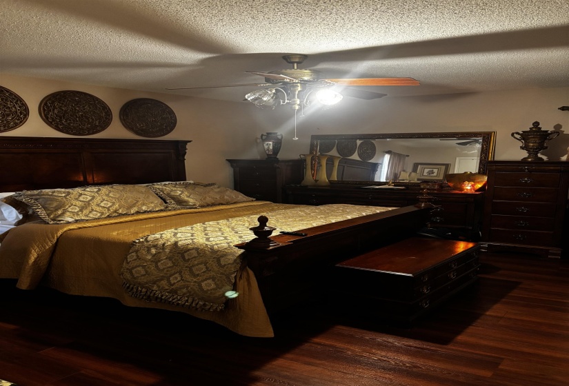 Warm bedroom featuring dark wood-finish flooring, a built-in ceiling fan with integrated lighting, and a dark wood bed frame with intricate headboard detailing