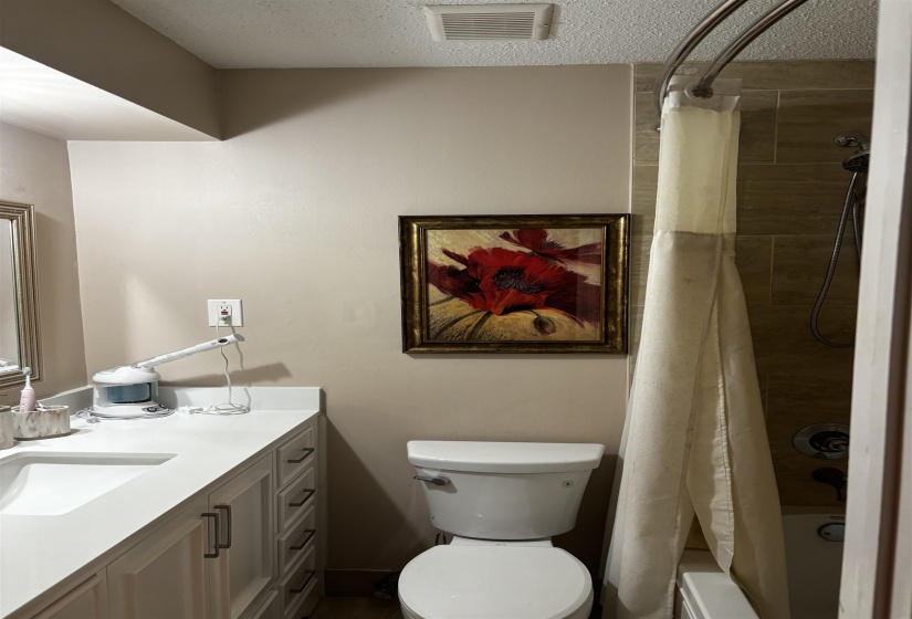 Bathroom featuring a white vanity with an integrated sink, a white toilet, and a tiled shower with a curved shower rod