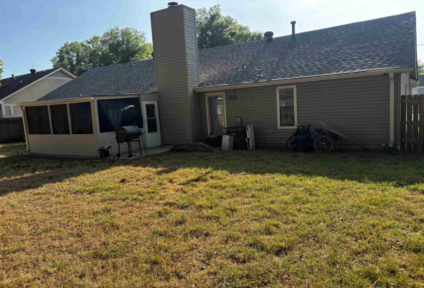 Expansive backyard featuring a screened porch, a prominent chimney, horizontal siding, and a partial wood fence
