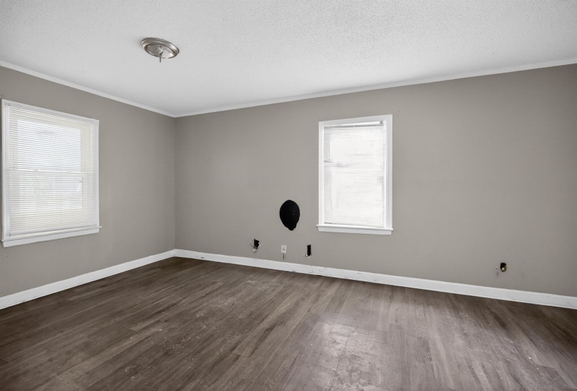 Spacious interior room featuring wood-finish flooring, two windows with blinds, a ceiling-mounted light fixture, and neutral painted walls
