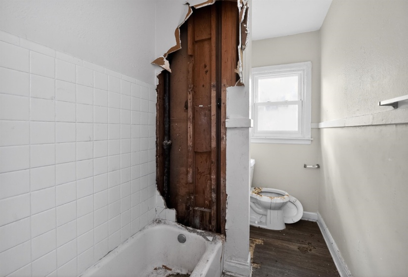 Bathroom space featuring white square wall tiles, a white bathtub, a single pane window, and wood-finish flooring