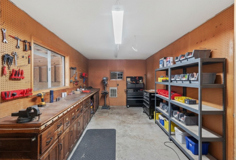 Dedicated workshop with pegboard walls, extensive workbench space, shelving, and wall-mounted heating and cooling (conveyed as-is). Virtually staged.