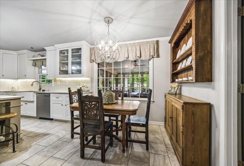 Bright kitchen and dining area featuring white cabinetry, a farmhouse sink, stainless steel dishwasher, and tile flooring