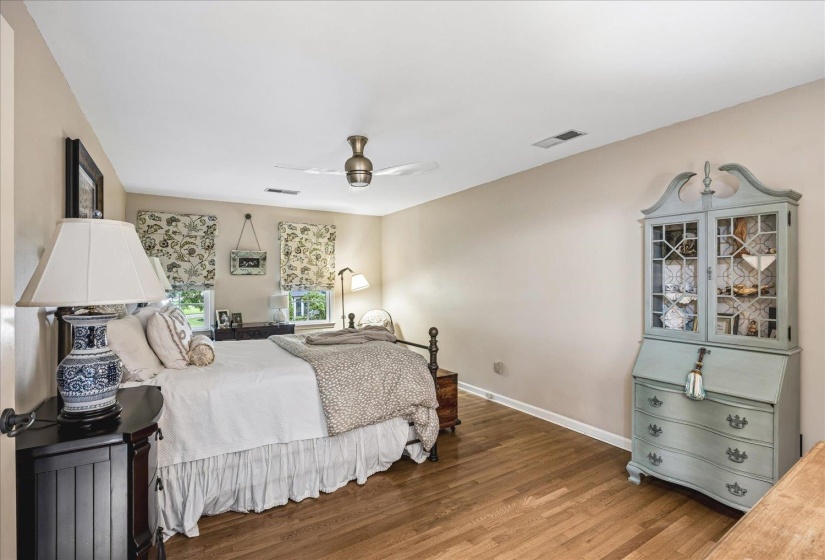 Light-toned walls complement wood-finish flooring in this room featuring a ceiling fan, recessed lighting, and dual windows
