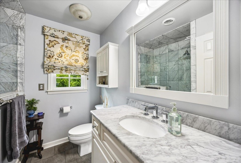 Bathroom featuring a marble-tile shower enclosure, vanity with marble countertop, and an undermount sink