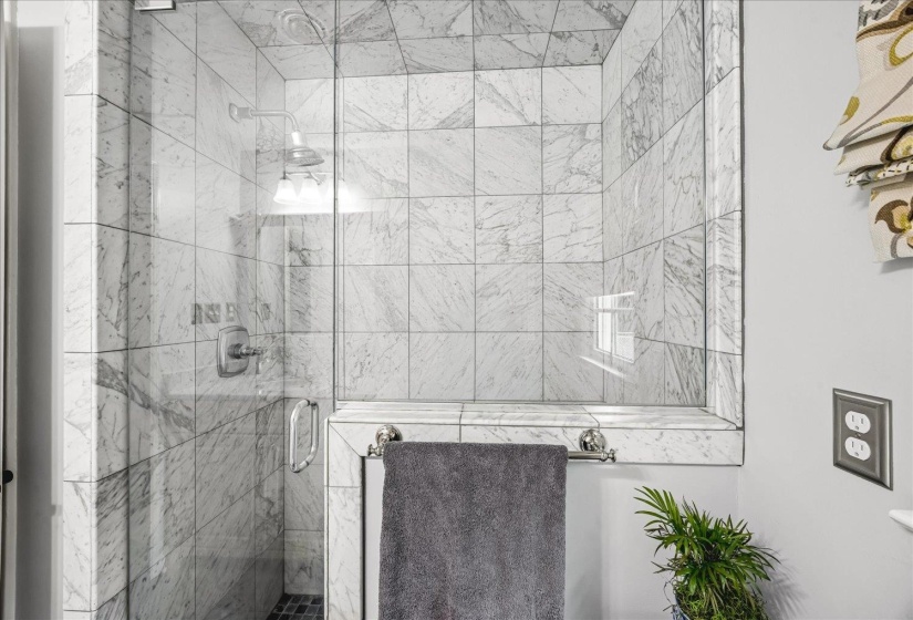 Walk-in shower with clear glass enclosure, full-height marble tile surround, built-in tile bench, and mosaic tile flooring