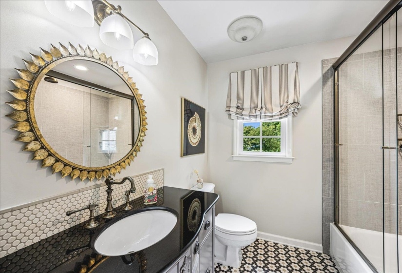 Bathroom featuring a dark vanity with an integrated sink, a sunburst-style mirror, and a tile backsplash